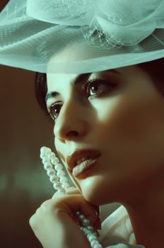 Thoughtful young female in white headwear with pearl necklace and makeup looking away in light place