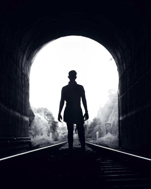 Silhouette of a Person in Black Jacket Standing on Tunnel