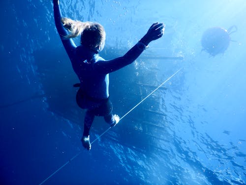 Anonymous woman diving underwater of blue sea