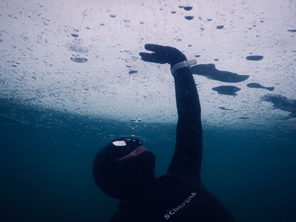 Free Anonymous diver in mask and wetsuit touching solid ice while swimming under seawater during freediving Stock Photo