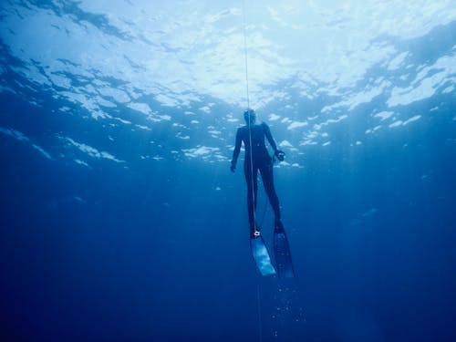 Anonymous person in flippers diving underwater of blue ocean