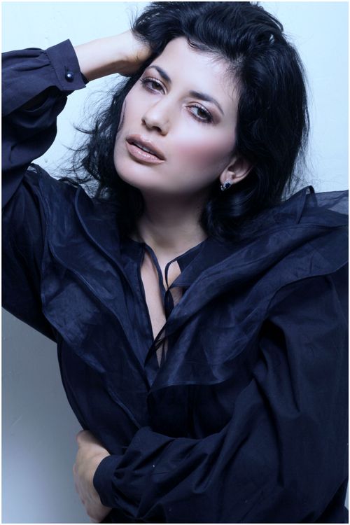 Free Portrait of a sophisticated woman wearing an elegant black blouse, posing with hand on head, indoors. Stock Photo