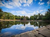Calm waters mirroring Neak Pean Temple and lush greenery under a vibrant blue sky in Cambodia.