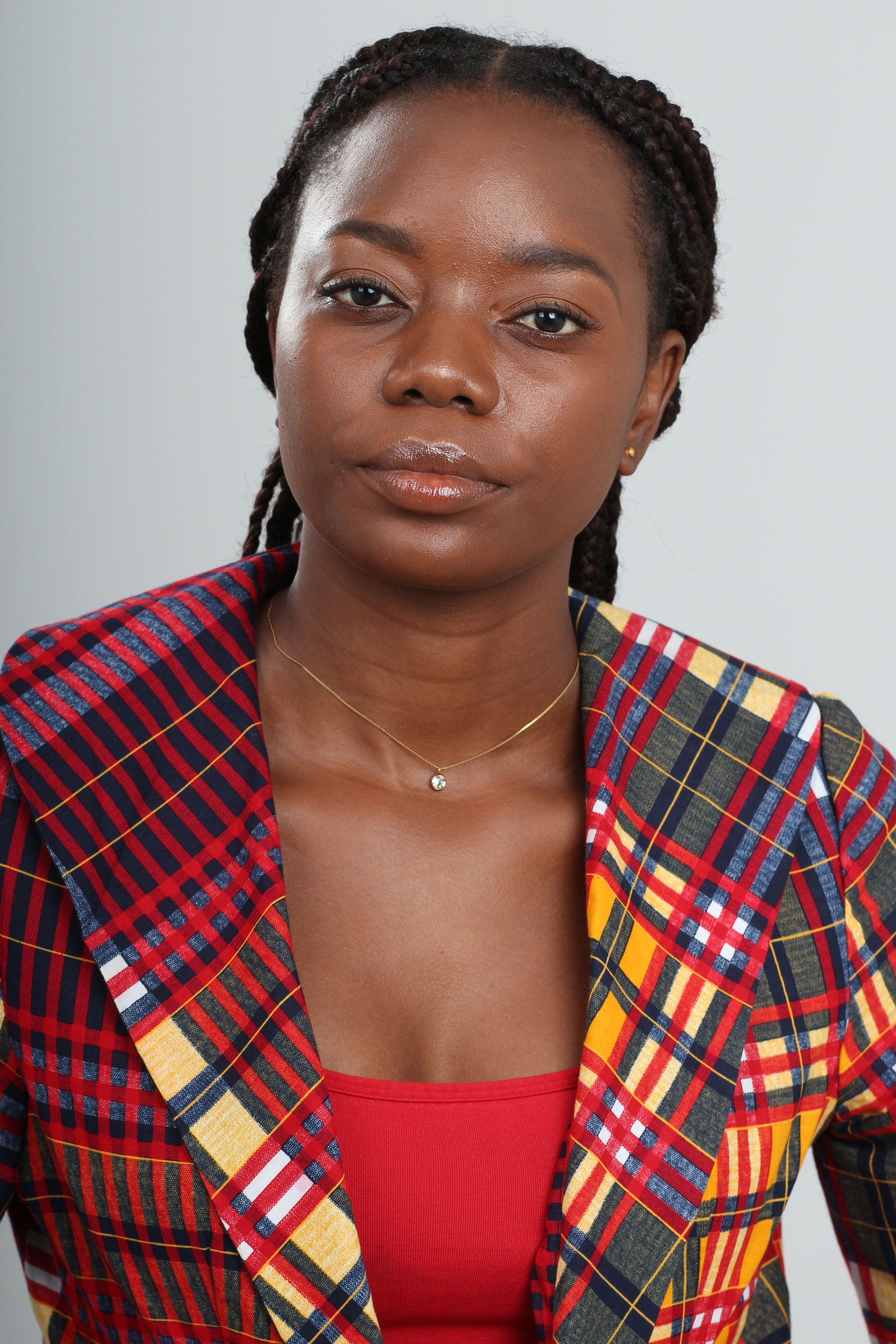 A close-up portrait of an African woman in a colorful plaid blazer, looking confidently at the camera.