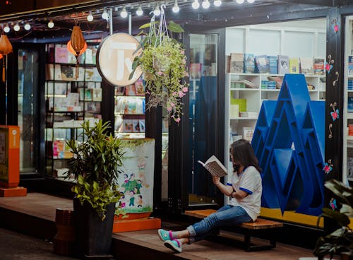 Woman Sitting Down On Bench And Reading Infront of Store