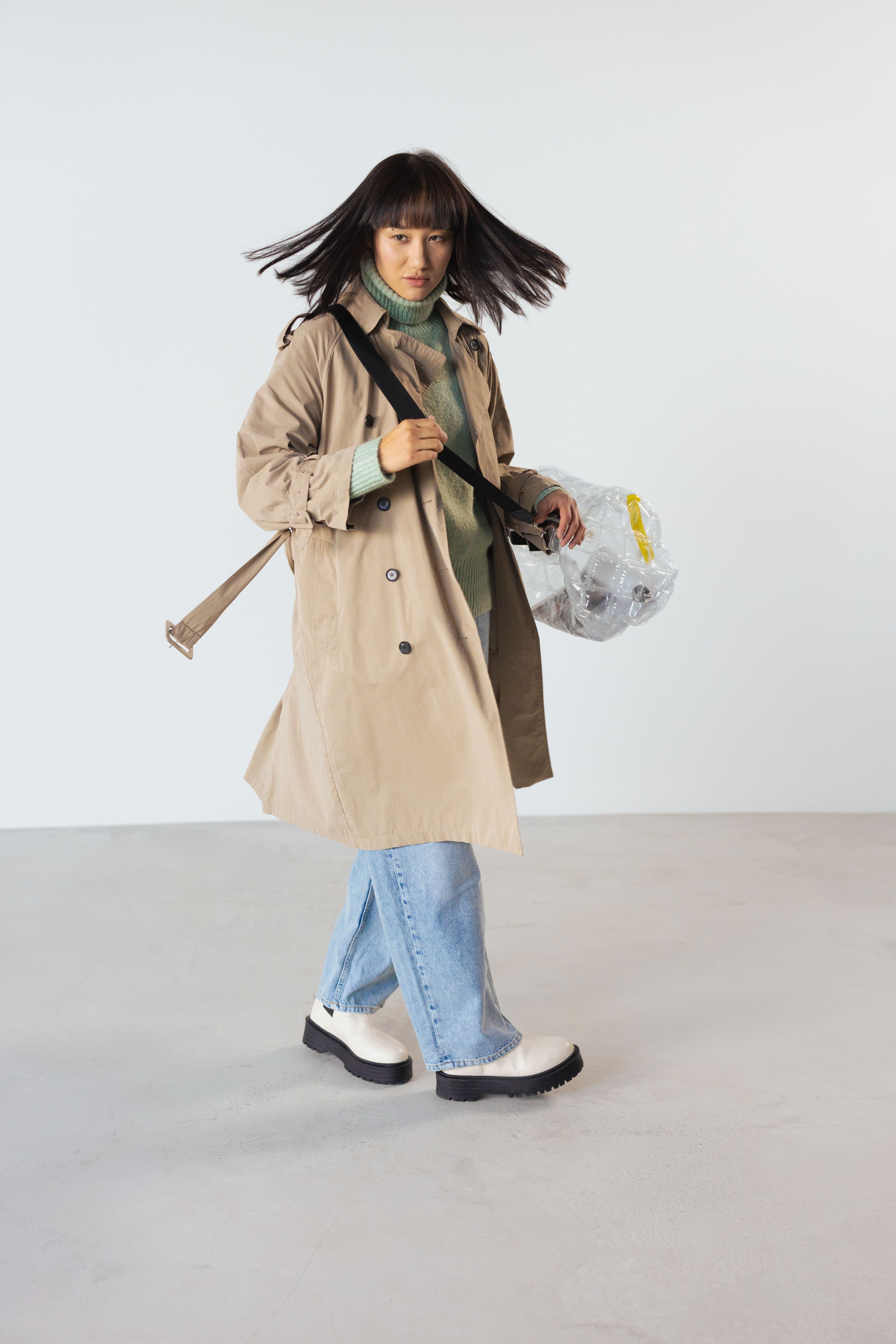 Jovem estilosa em um trench coat e jeans denim posando em ambiente interno para uma sessão de moda.
