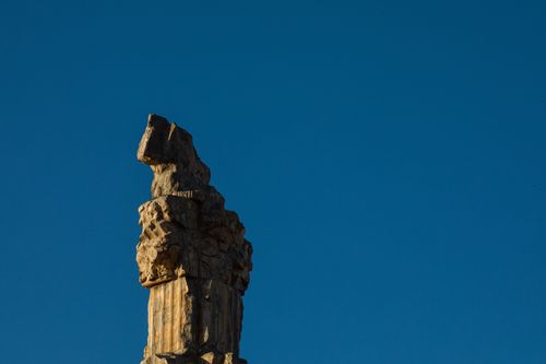 Free Detailed view of an ancient Persian stone pillar under a vivid blue sky, highlighting intricate designs. Stock Photo