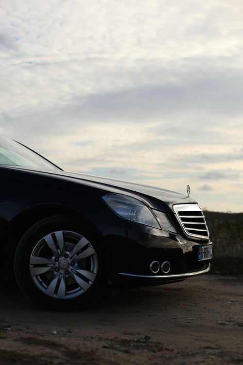 Free Close-up of a black luxury car parked on a rural road with a dramatic sky. Stock Photo
