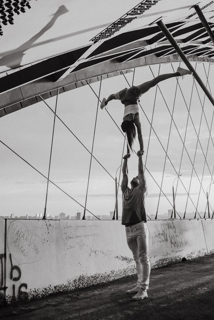 Gymnastic Woman And Man Doing Trick On Bridge