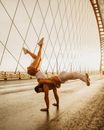 Full body of energetic anonymous man and woman doing counterbalance pose of dance on asphalt road of huge bridge in sunlight