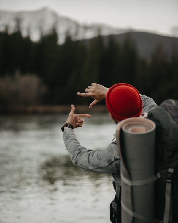Free Unrecognizable backpacker making hands frame gesture on lakeside Stock Photo