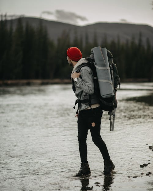 Free Side view full body of anonymous male tourist with backpack strolling on lake against tall trees during trip in nature Stock Photo