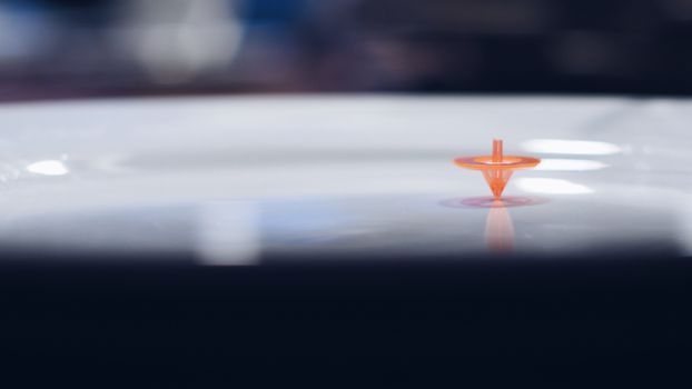 Close-up of an orange spinning top creating a reflective shadow on a glossy surface.