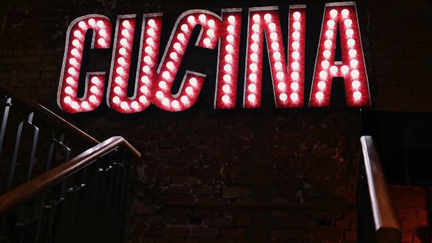 Glowing 'CUCINA' neon sign in a dimly lit, atmospheric restaurant setting with brick wall backdrop.
