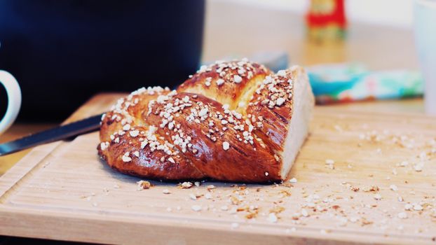Freshly baked challah bread on a wooden board, sprinkled with coarse sugar, indoors.