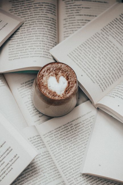 From above of glass of latte with art on foam on heap of opened books