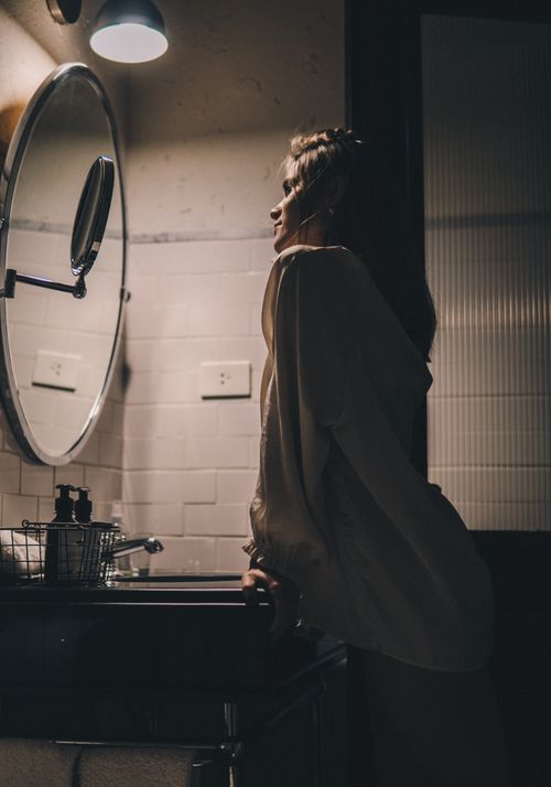 Free Silhouette of a woman in a dimly lit bathroom, reflecting in a round mirror. Stock Photo