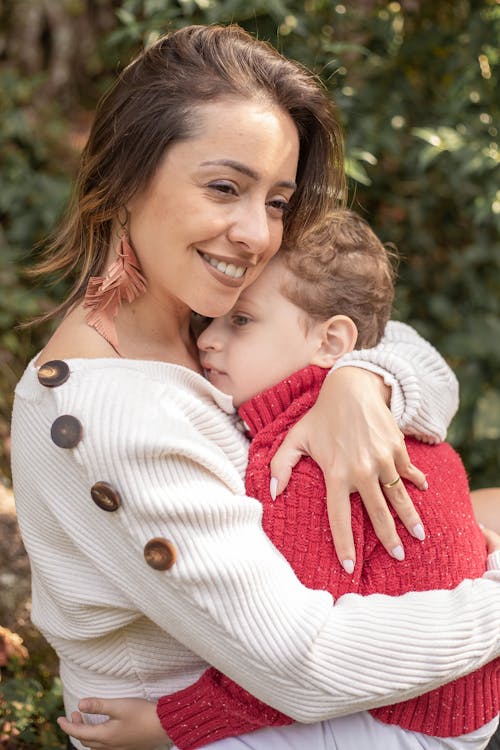 Photo of a Woman in a White Sweater Smiling while Hugging Her Child