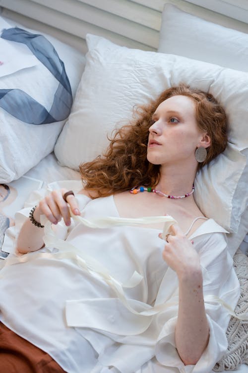 Woman in White Blouse Lying on Bed while Looking Afar