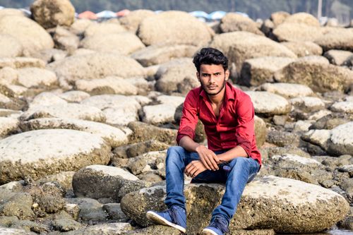 Free Young man in red shirt sitting on rocks at a beach in daylight. Stock Photo
