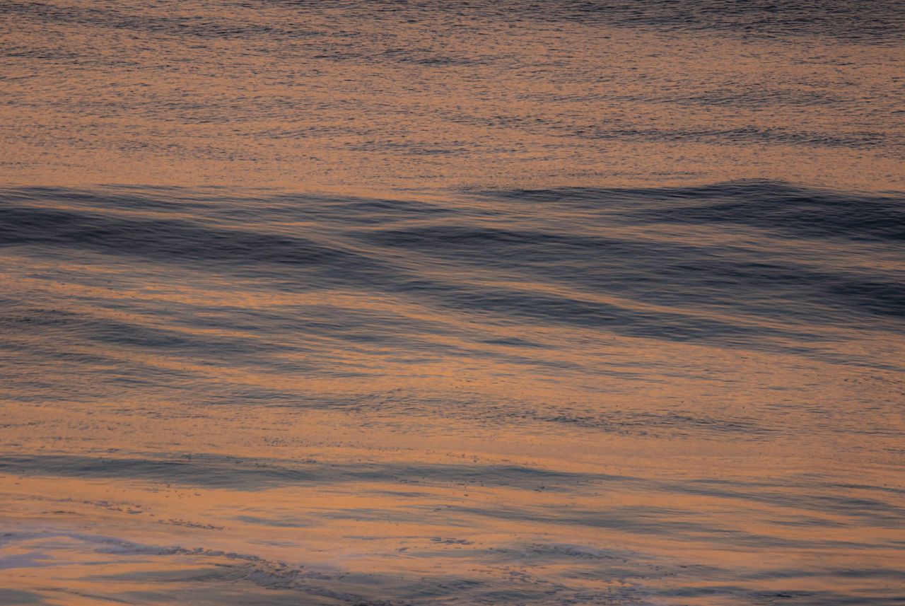 a tranquil scene of ocean waves with a warm glow at twilight creating