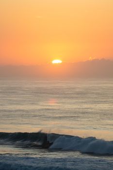 Breathtaking sunset over the ocean with dramatic waves crashing on the shore.