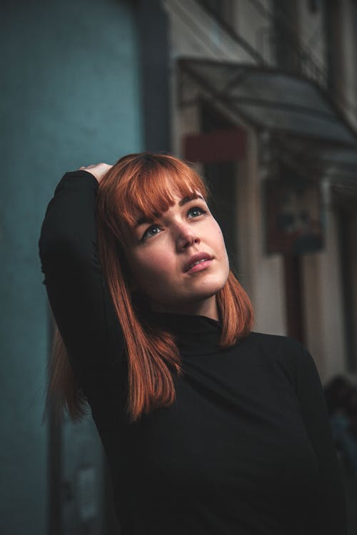 Selective Focus Photo of a Woman Looking Up While Touching Her Red Hair