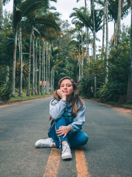 Free Casual portrait of a woman sitting on a road surrounded by palm trees in a tropical setting. Stock Photo