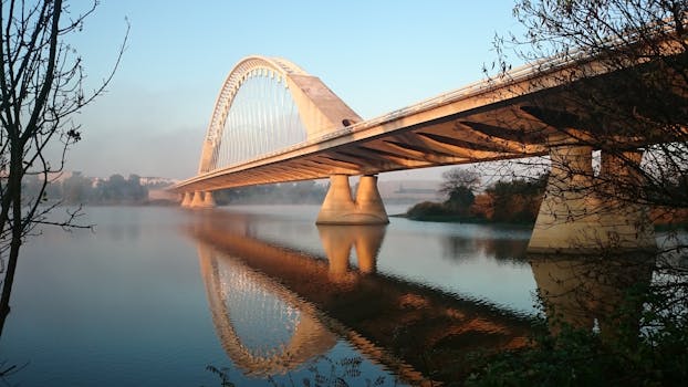 日出时分，平静的河面上倒映着一座琴弦拱门的宁静景色