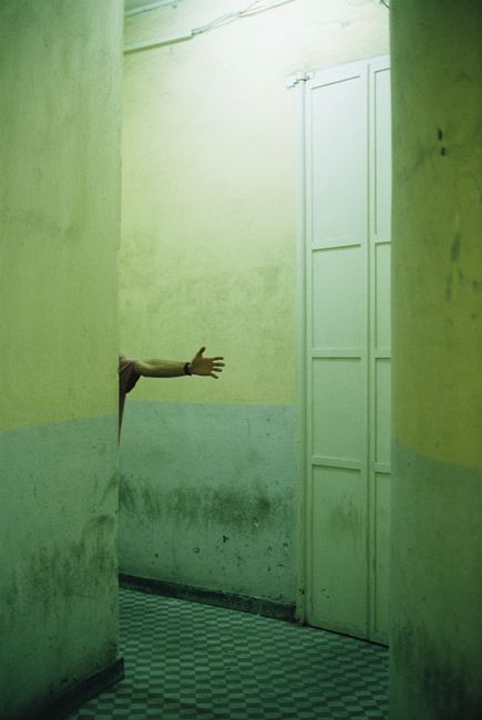 A person's arm reaches out in an unrecognizable hallway with concrete walls and a checkered floor.