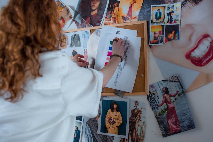 A Woman Putting Sketch Designs On A Corkboard