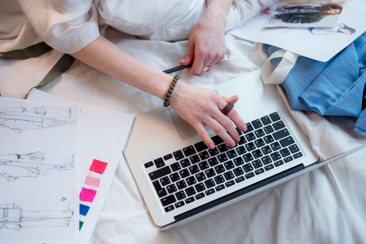 Hands working on a laptop surrounded by fashion sketches, embodying creative remote work.