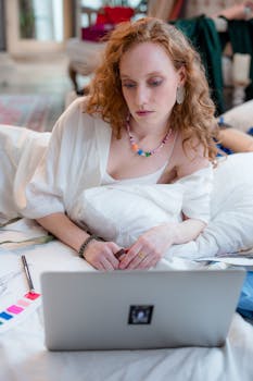 Fashionable woman lying on bed working with a laptop, indoors.