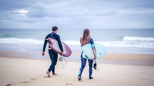 Man and Woman Walking on the Sea Shore while Carrying Surfboards 