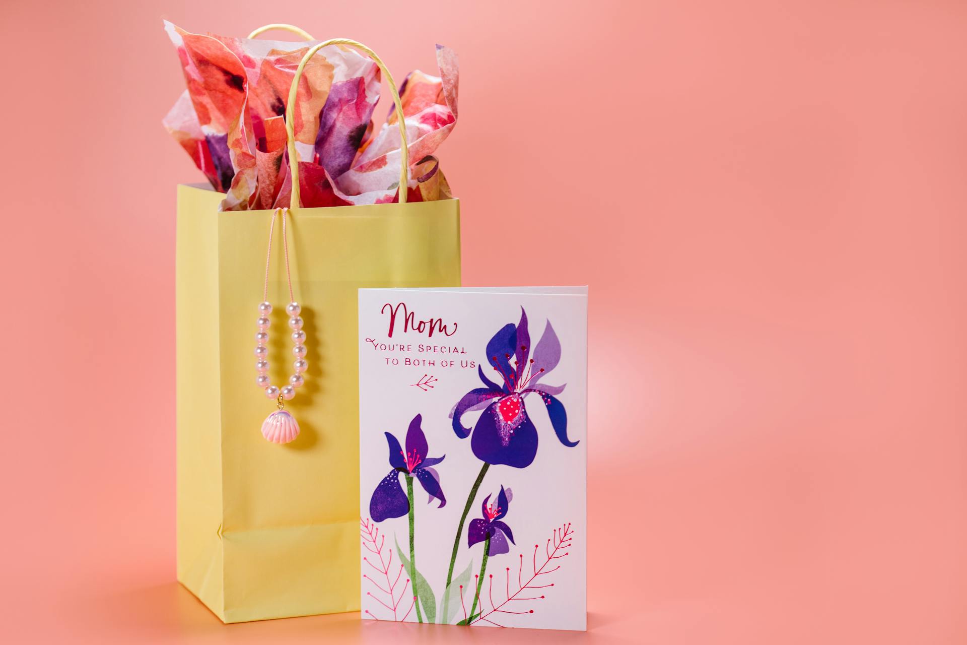 A yellow gift bag with a Mother's Day card and bracelet on a pink background, perfect for celebration themes.