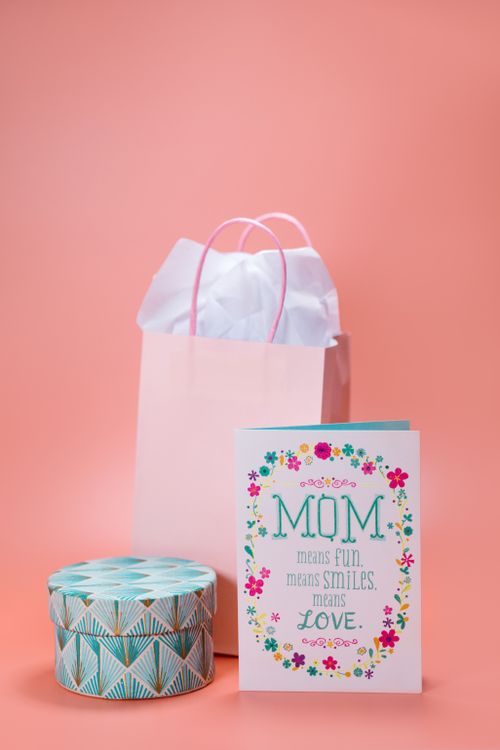 Free Charming Mother's Day setup with a greeting card, gift bag, and decorative box on a pastel pink background. Stock Photo