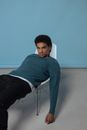 A Man Wearing a Blue Sweater and Black Pants Slouching on Chair