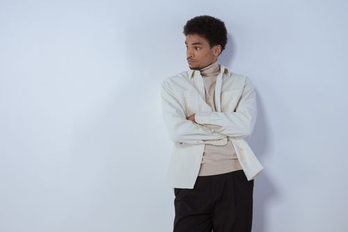 Free Young man in white shirt and turtleneck leaning against a wall with arms crossed. Stock Photo