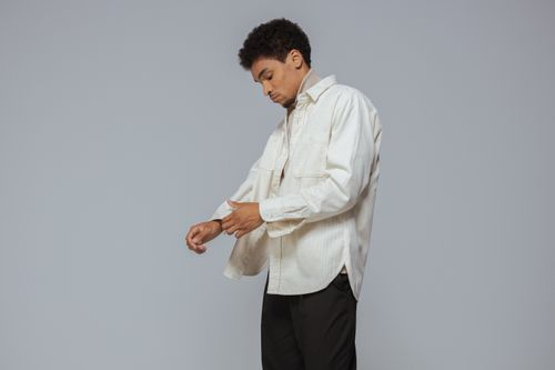 Free A young man rolls up sleeves of a casual white shirt, looking focused and stylish. Stock Photo