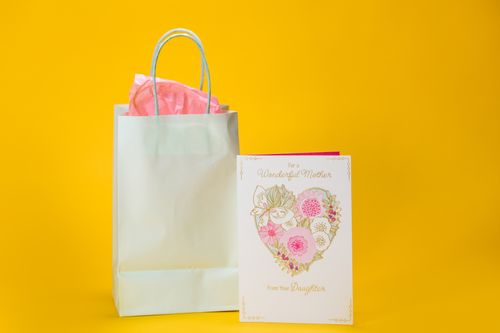 Free A beautifully designed Mother's Day card and gift bag on a vibrant yellow background, perfect for celebrating a special occasion. Stock Photo