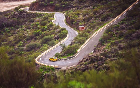 A yellow car navigates a winding mountain road in Santa Cruz de Tenerife, Spain.