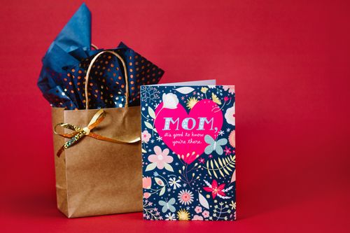Free A colorful Mother's Day card with floral design and gift bag on vibrant red background. Stock Photo