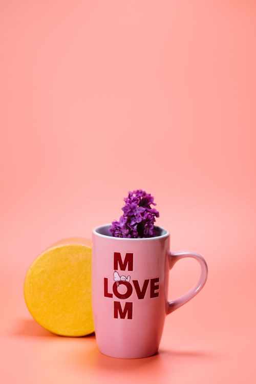 Free Pink mug with 'Love Mom' text filled with purple flowers on pink background. Stock Photo