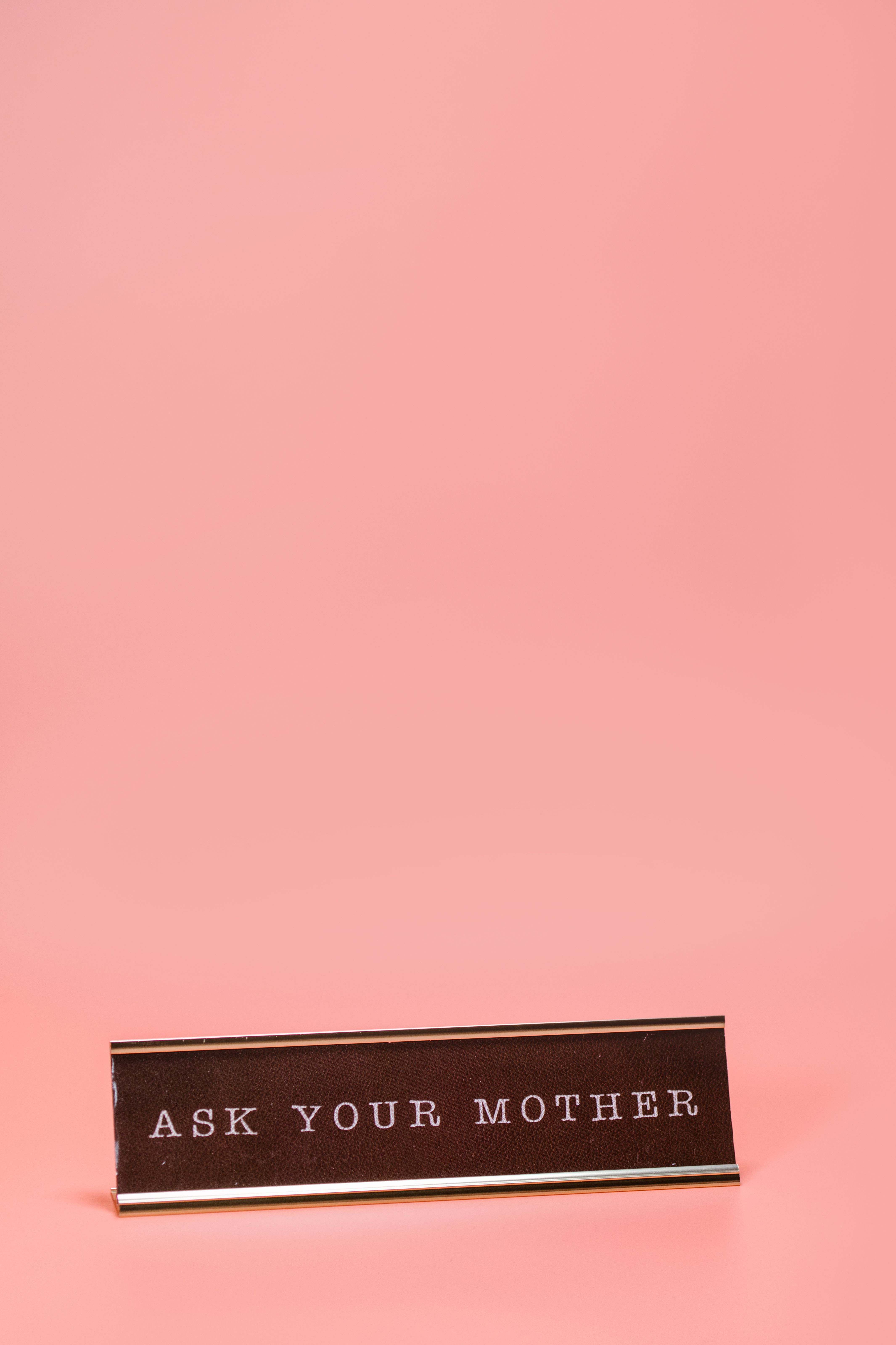 Humorous desk sign displaying text 'Ask Your Mother' with pink background.