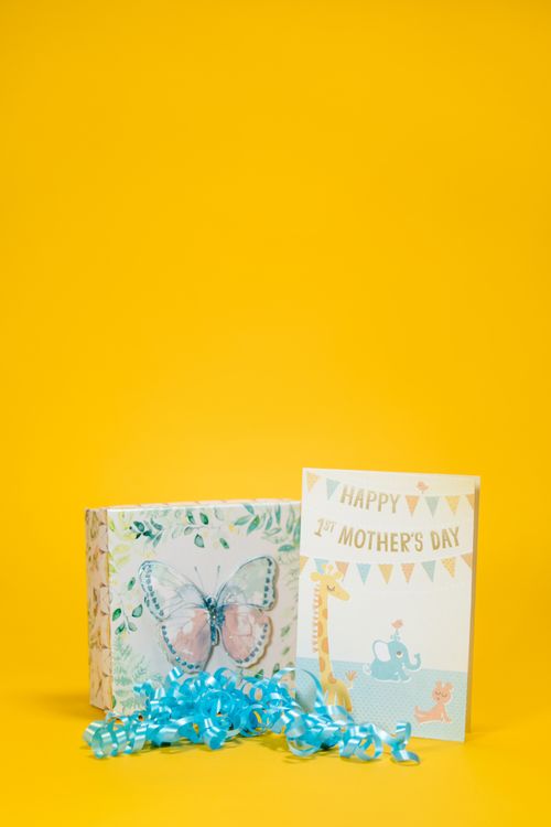 Free Mother's Day gift featuring a butterfly-themed box, greeting card, and ribbon on a yellow background. Stock Photo