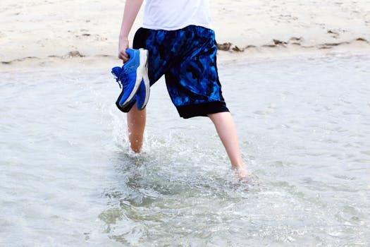 A person holding shoes walks barefoot in the water at Hampton Beach, NH.