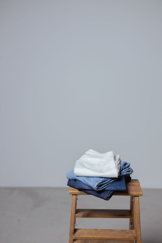 Folded white and blue jeans stacked on a wooden stool, photo by cottonbro studio on Pexels