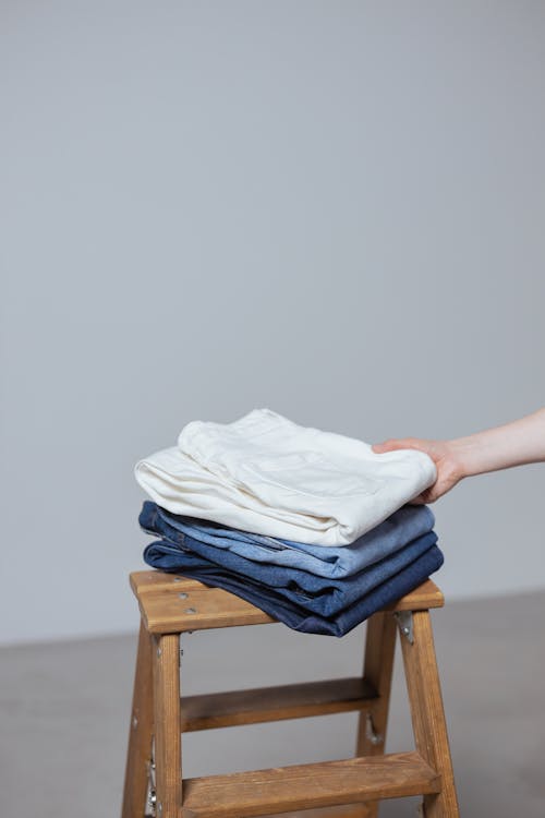 Free A neatly folded stack of blue jeans and a white shirt on a wooden ladder indoors. Stock Photo
