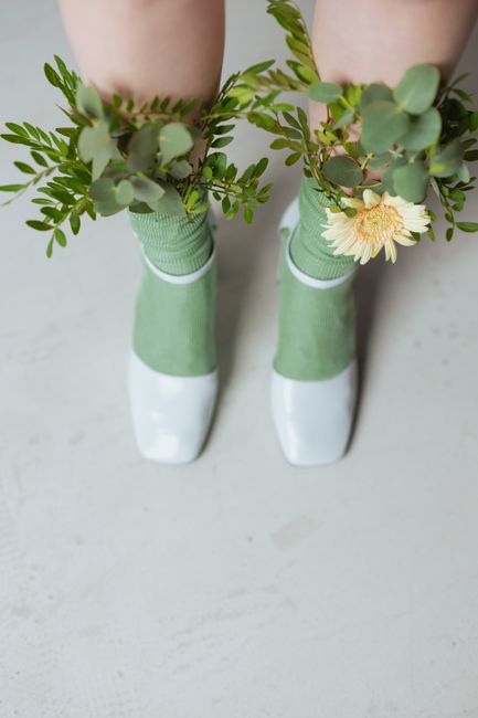 Top view of legs in green socks and silver shoes decorated with fresh flowers and leaves.