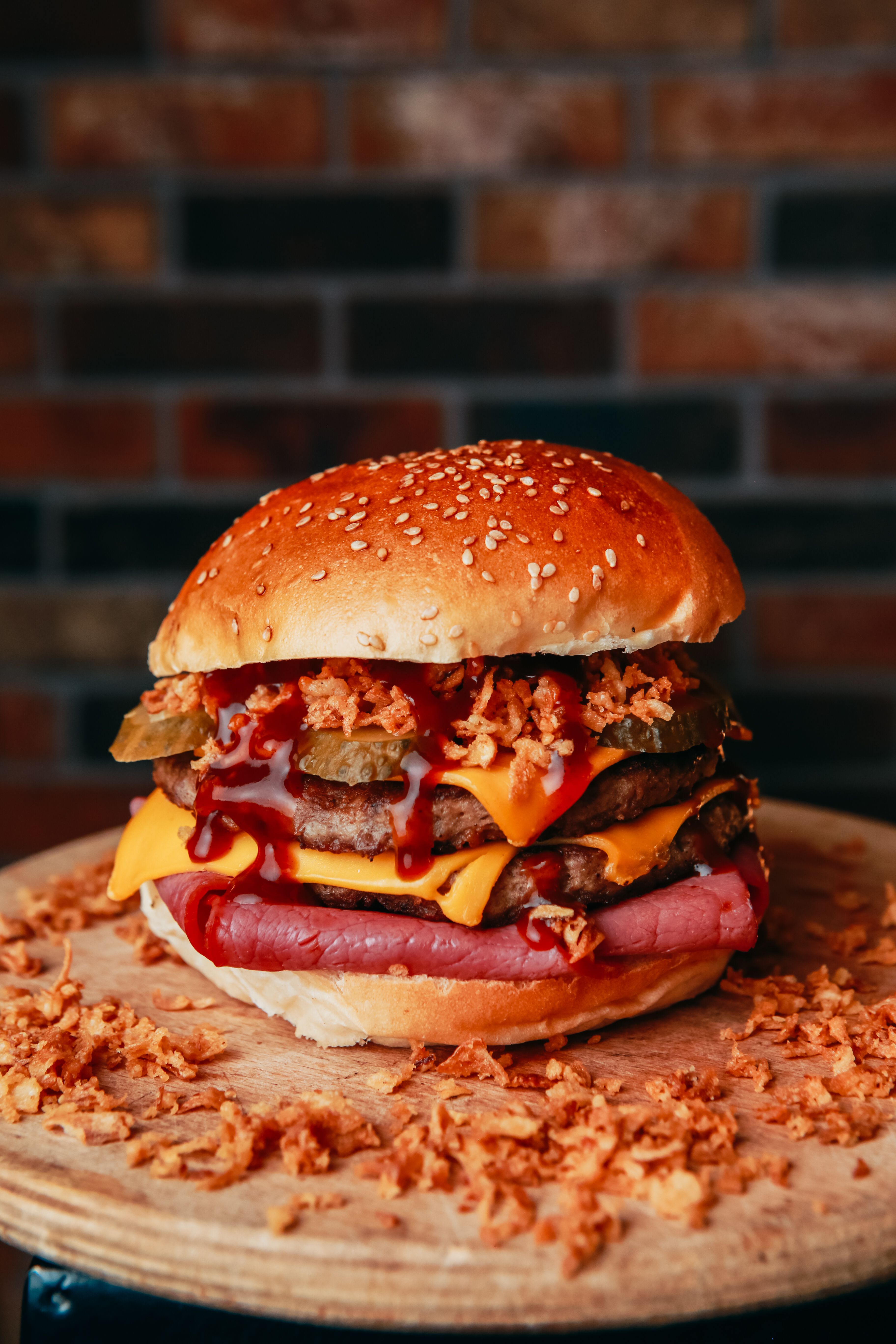 Delicious burger with cheese, bacon, and crispy toppings on a wooden plate.